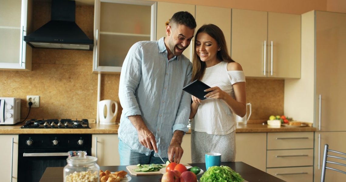 Attractive couple meet in the kitchen early morning. Handsome woman using tablet sharing his husband social media at home